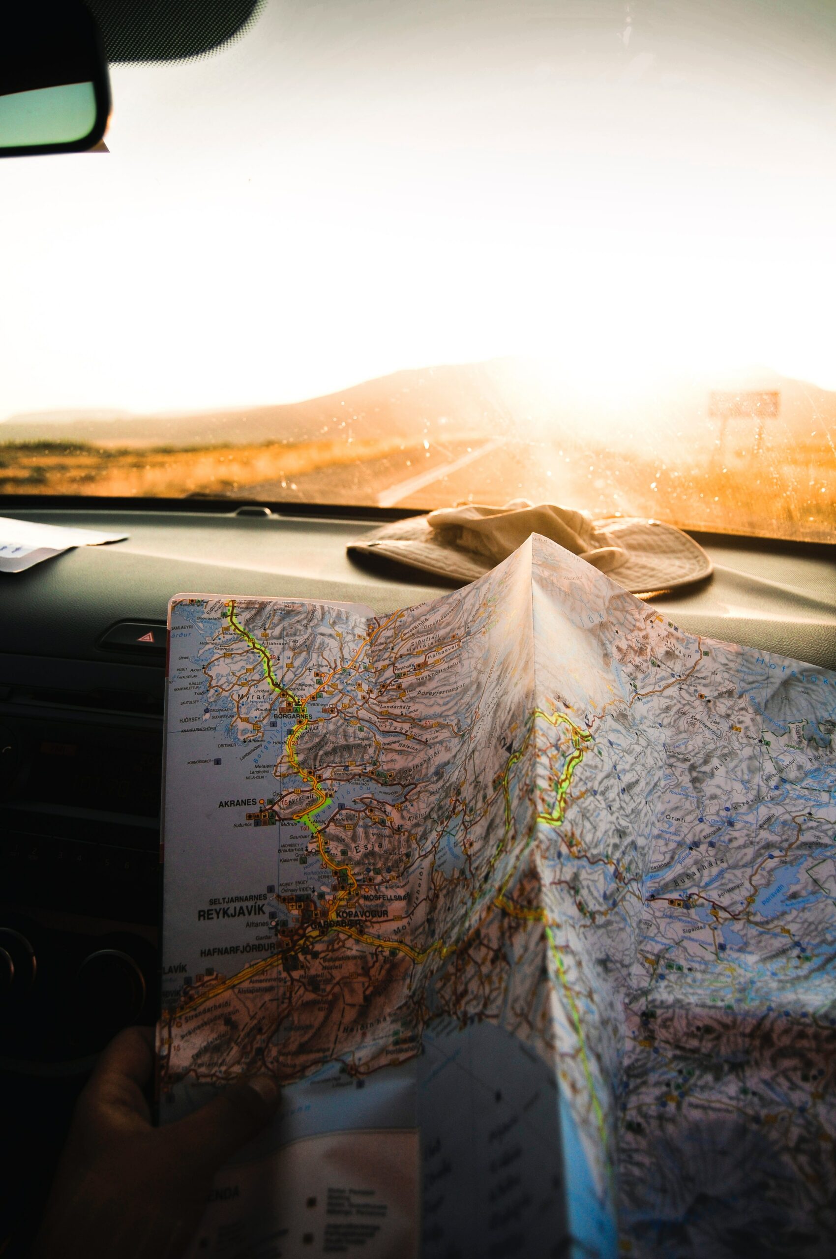 an unfolded map is laying against a vehicle dashboard that is driving towards a sunset